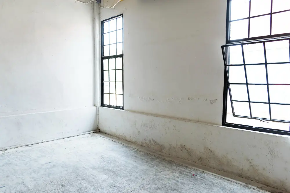An interior room with visible structural damage, showing a bulging wall and bent window frame.